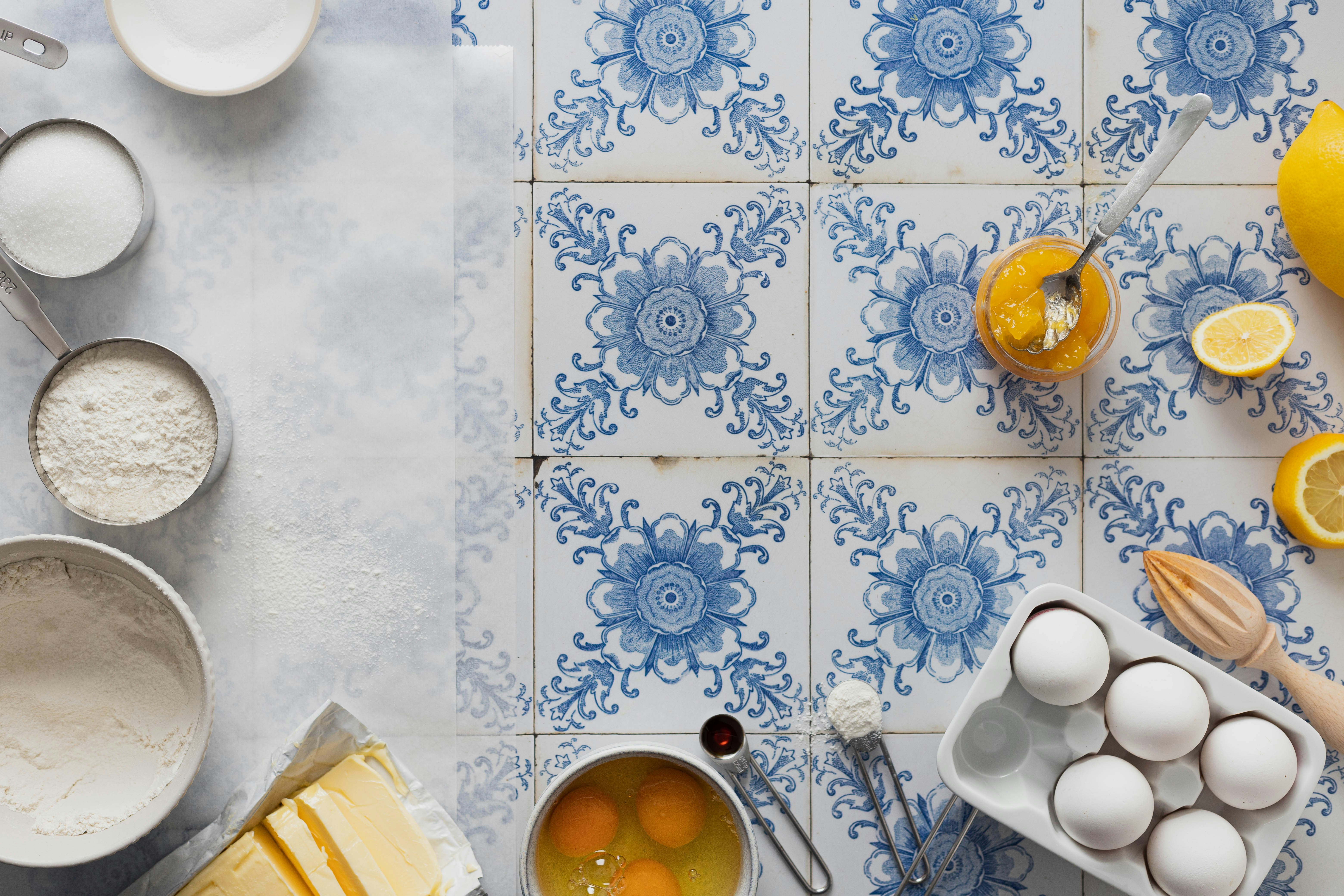 Five measuring spoons filled with flour, vanilla extract, cinnamon, sugar, and baking powder, arranged on a marble surface.